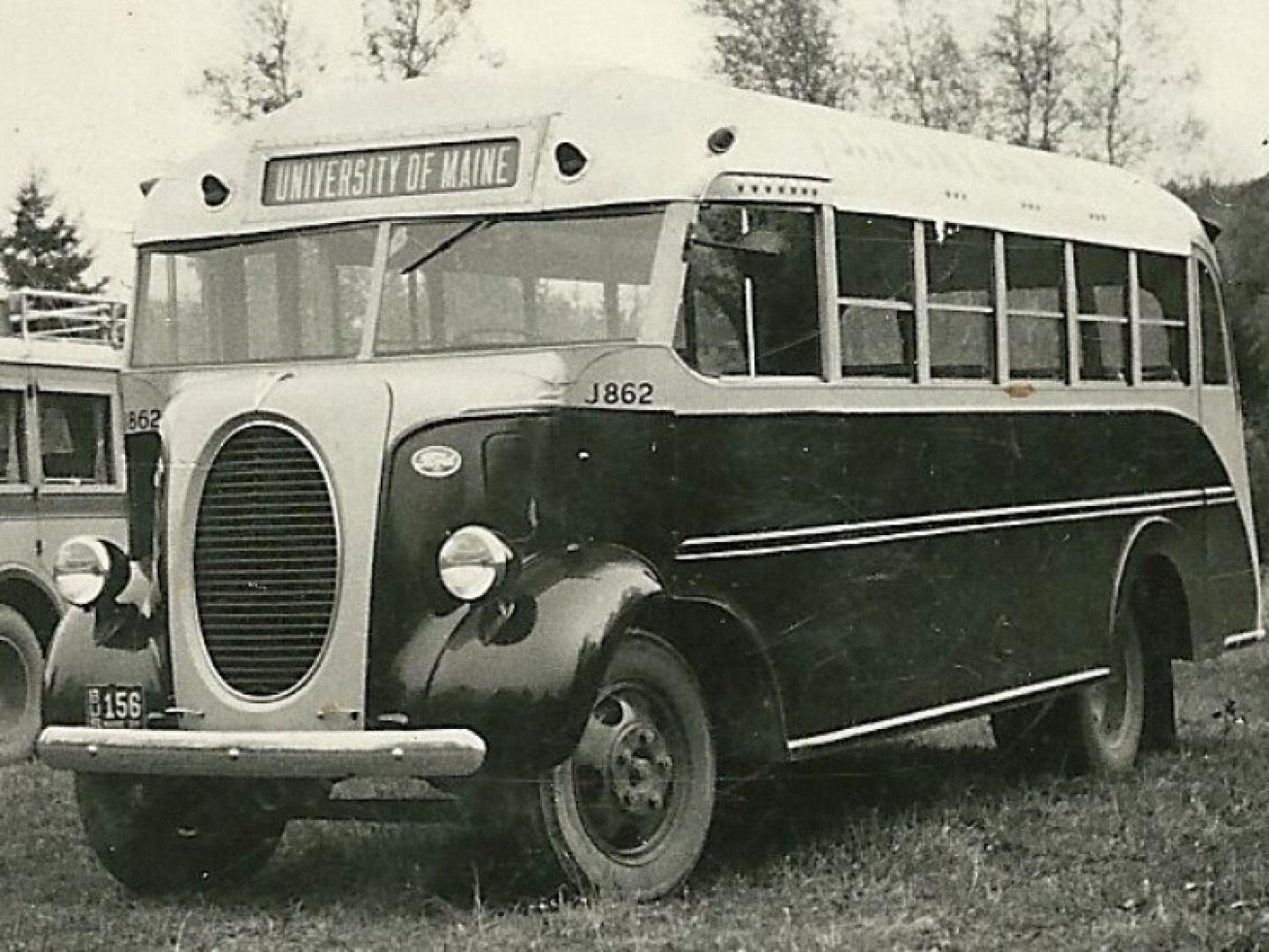 Vintage black-and-white bus parked outdoors on a dirt road, with rounded front and large windows