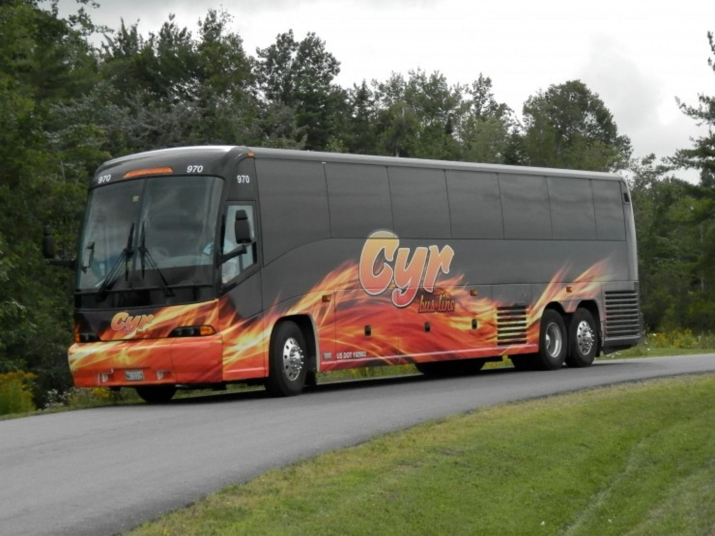 Black charter bus with orange flame graphics driving on a rural road