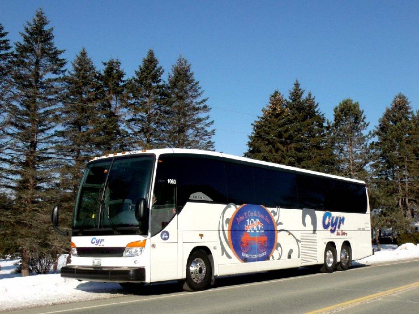 White tour bus parked in snow beside evergreen trees under a clear blue sky