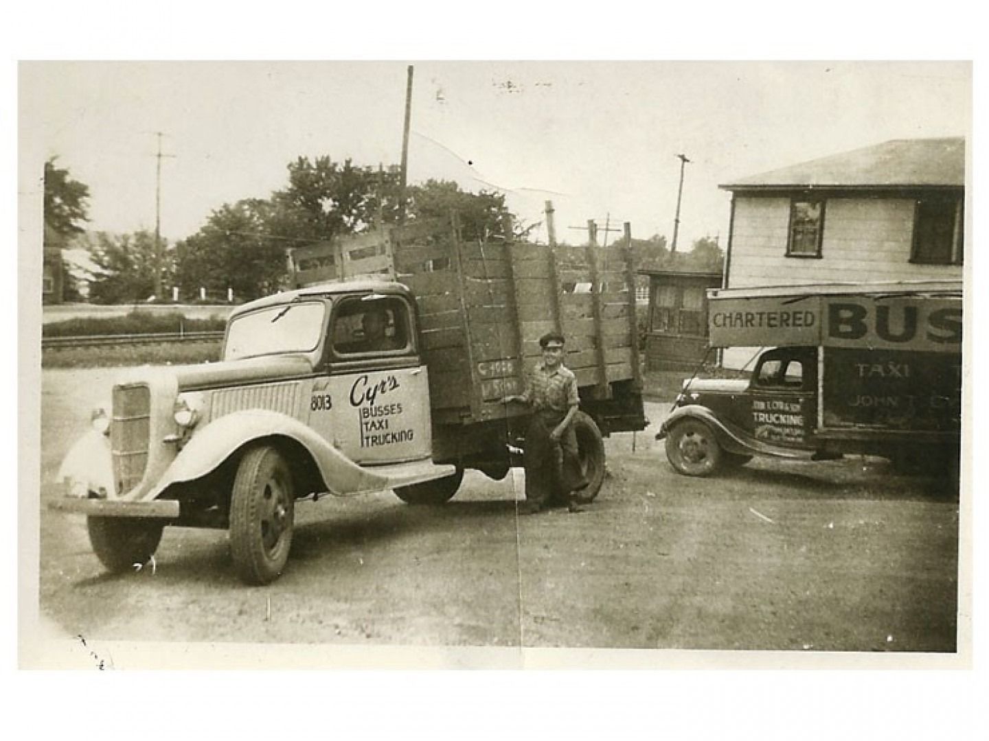 Vintage tow truck hauling an old car beside a bus station, with a man standing nearby.