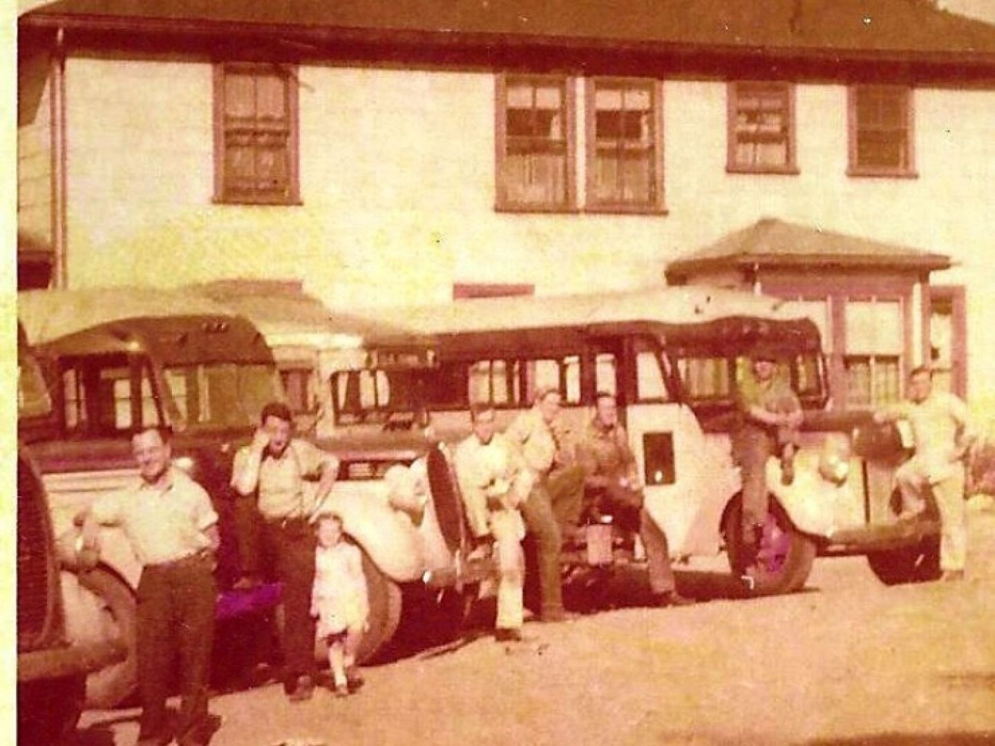 Group standing beside vintage vehicles in front of a building