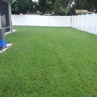 A well-manicured green lawn enclosed by a white privacy fence and a home's screened-in patio.