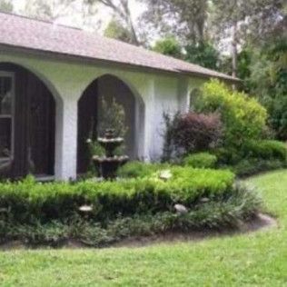 White house with arched entryway, fountain, and green landscaping.