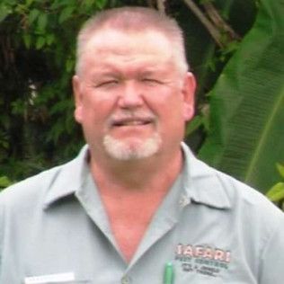 Man with short hair and goatee in a Safari Pest Control shirt. Outdoors with greenery in the background.