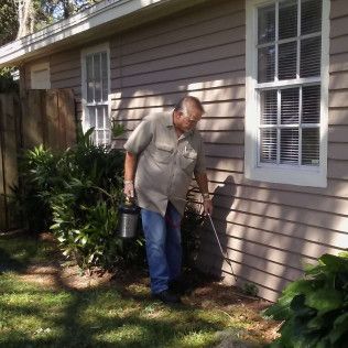 Man spraying insecticide along the side of a house, outdoors.