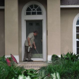 Person spraying insecticide at a house doorway.
