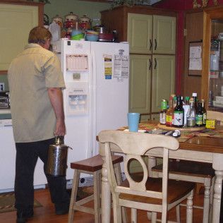 Man carrying metal container walking toward refrigerator in kitchen.