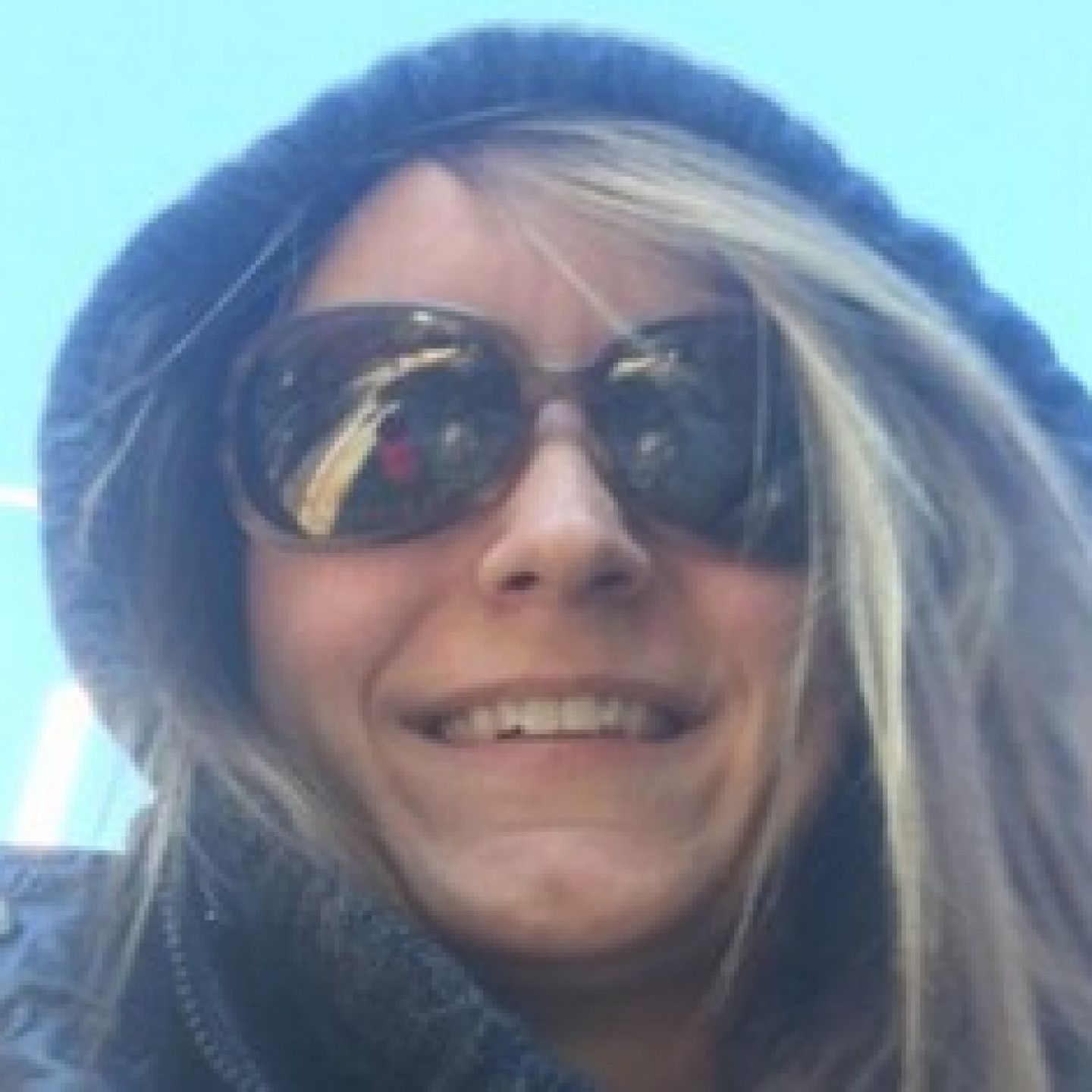 Woman wearing sunglasses and a hooded jacket, smiling outdoors.