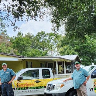 Two men in matching shirts stand by pest control trucks outside a building.