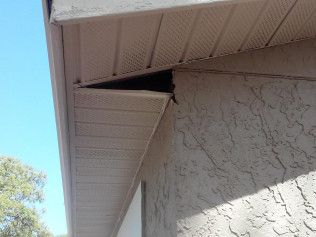 Tan soffit and fascia with triangular gap against stucco wall, blue sky.
