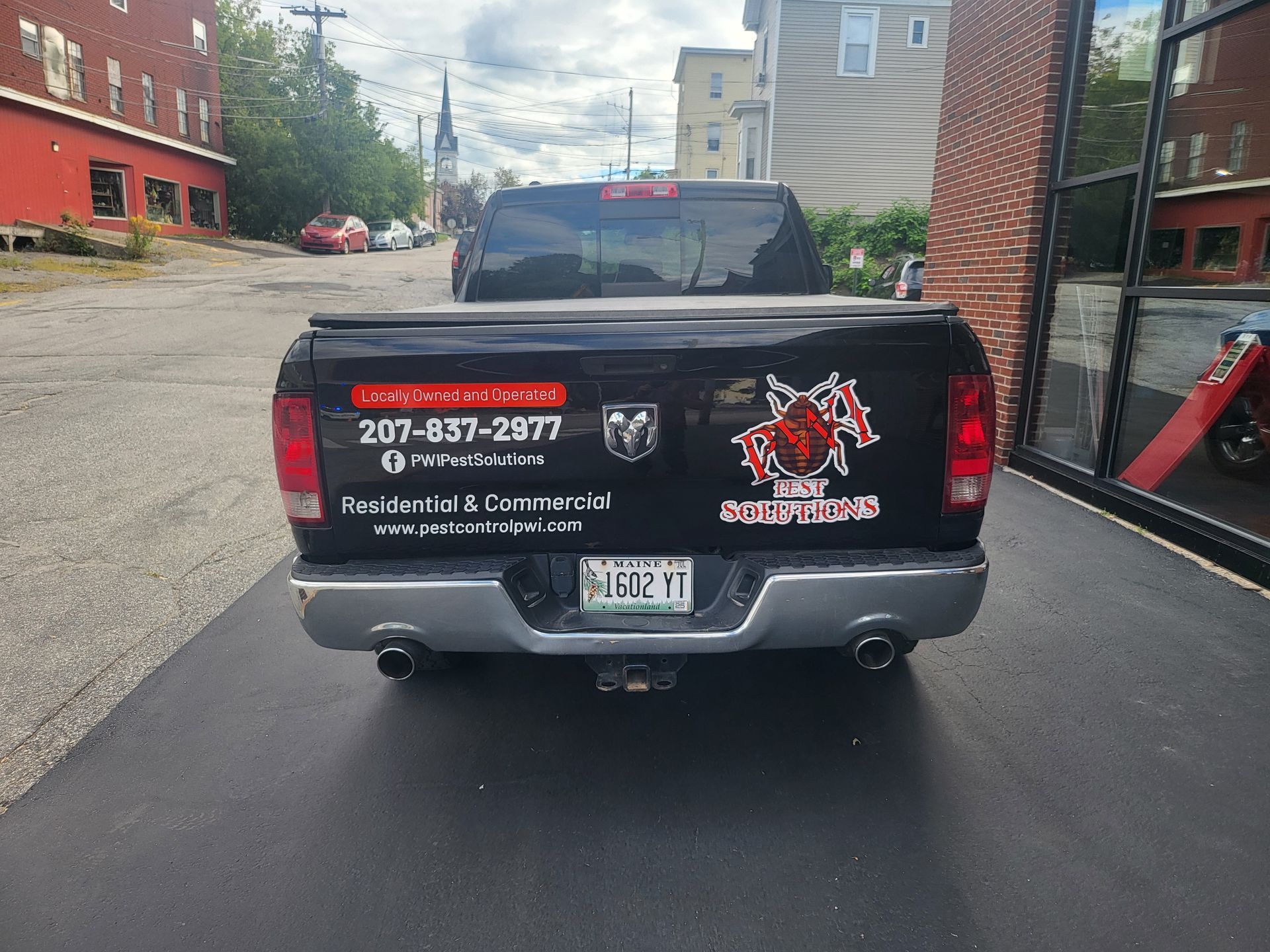 Black pickup truck with business decals parked in an alley between brick buildings.