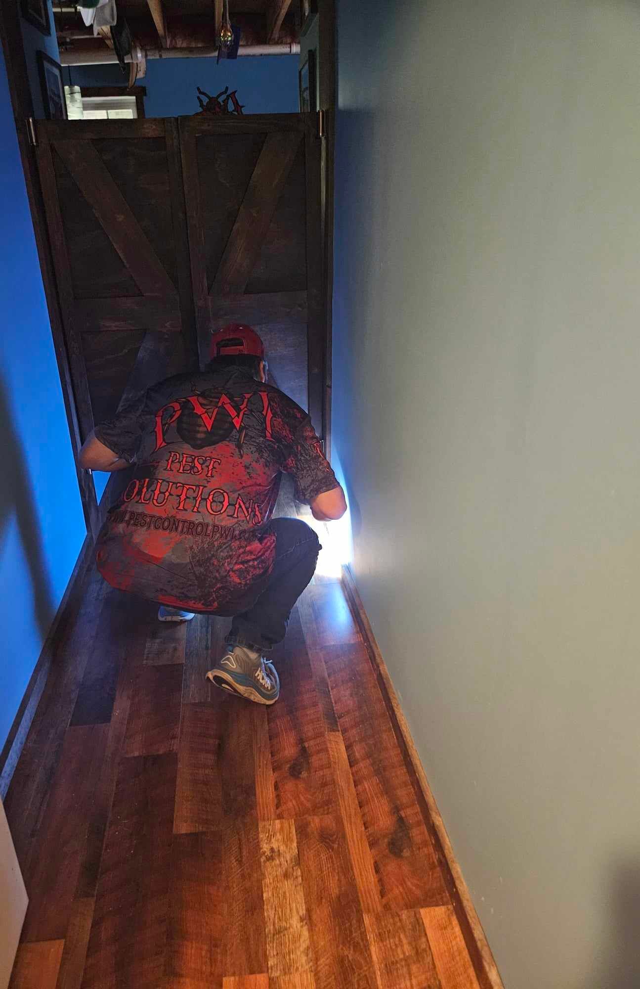 Person kneeling in a narrow hallway, reaching toward a bright light under a doorway.