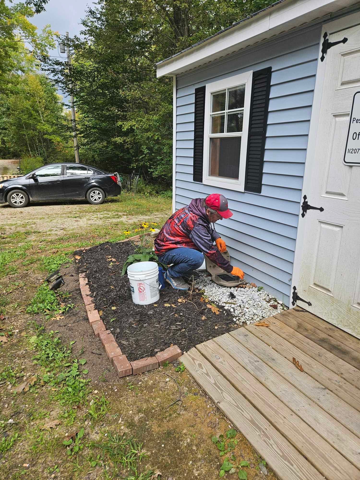 Person kneeling by a house foundation, installing stones beside blue siding and a white door.
