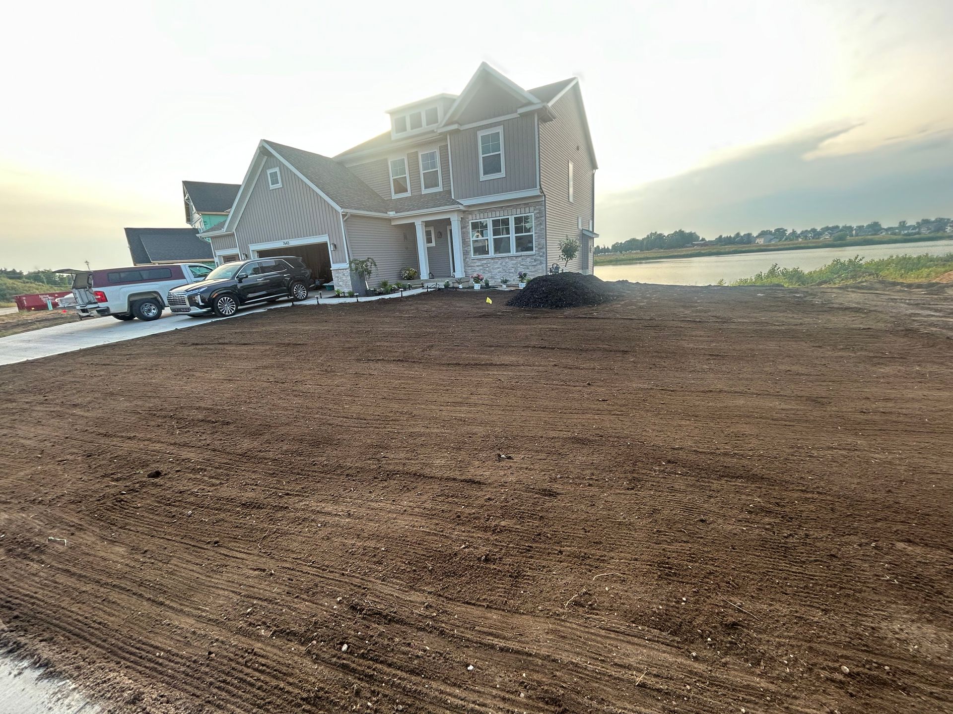 New beige house with a fresh dirt yard at sunset, overlooking a calm waterfront