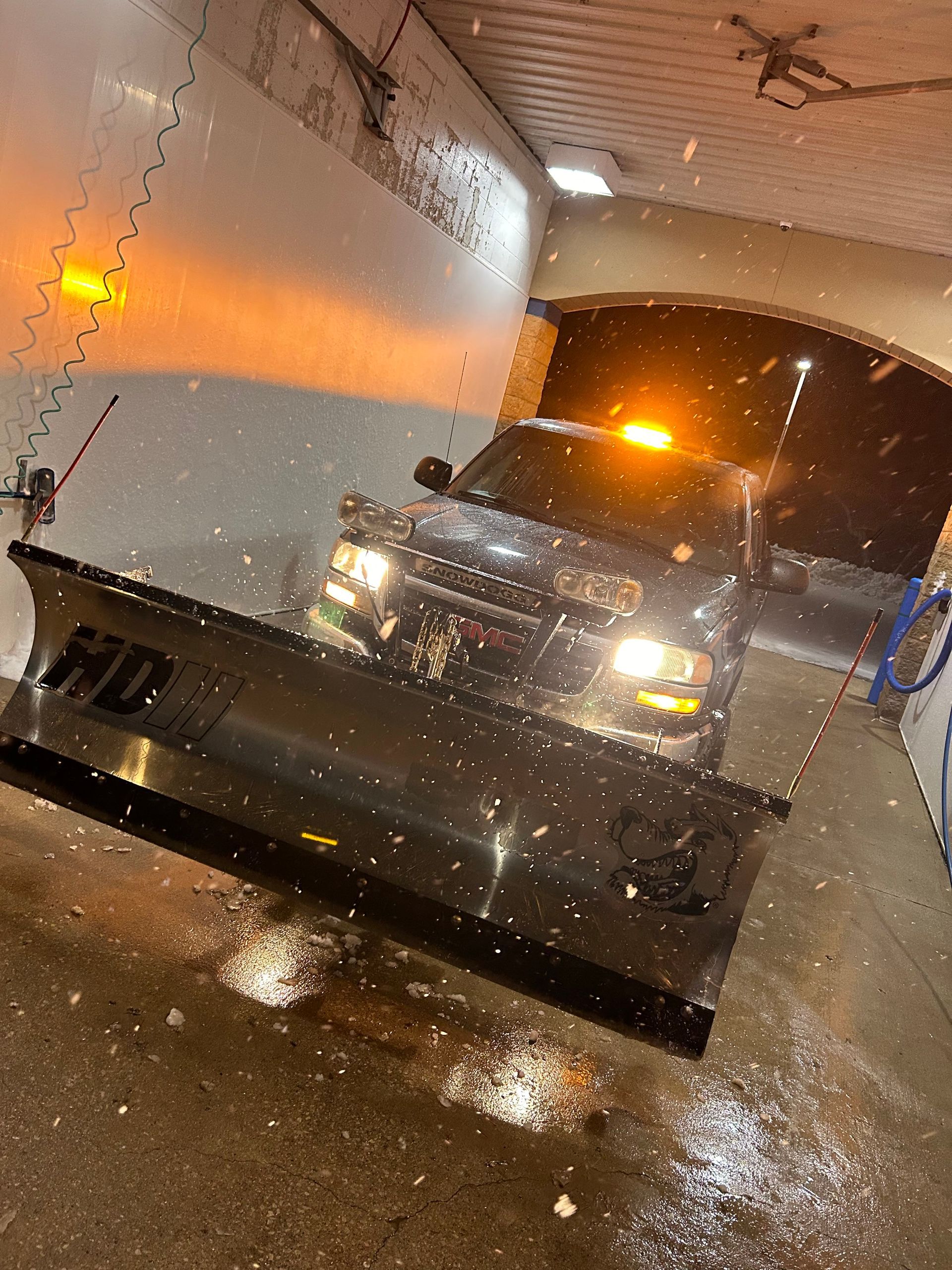 Snowplow in a wet tunnel, headlights on, clearing slushy snow at night