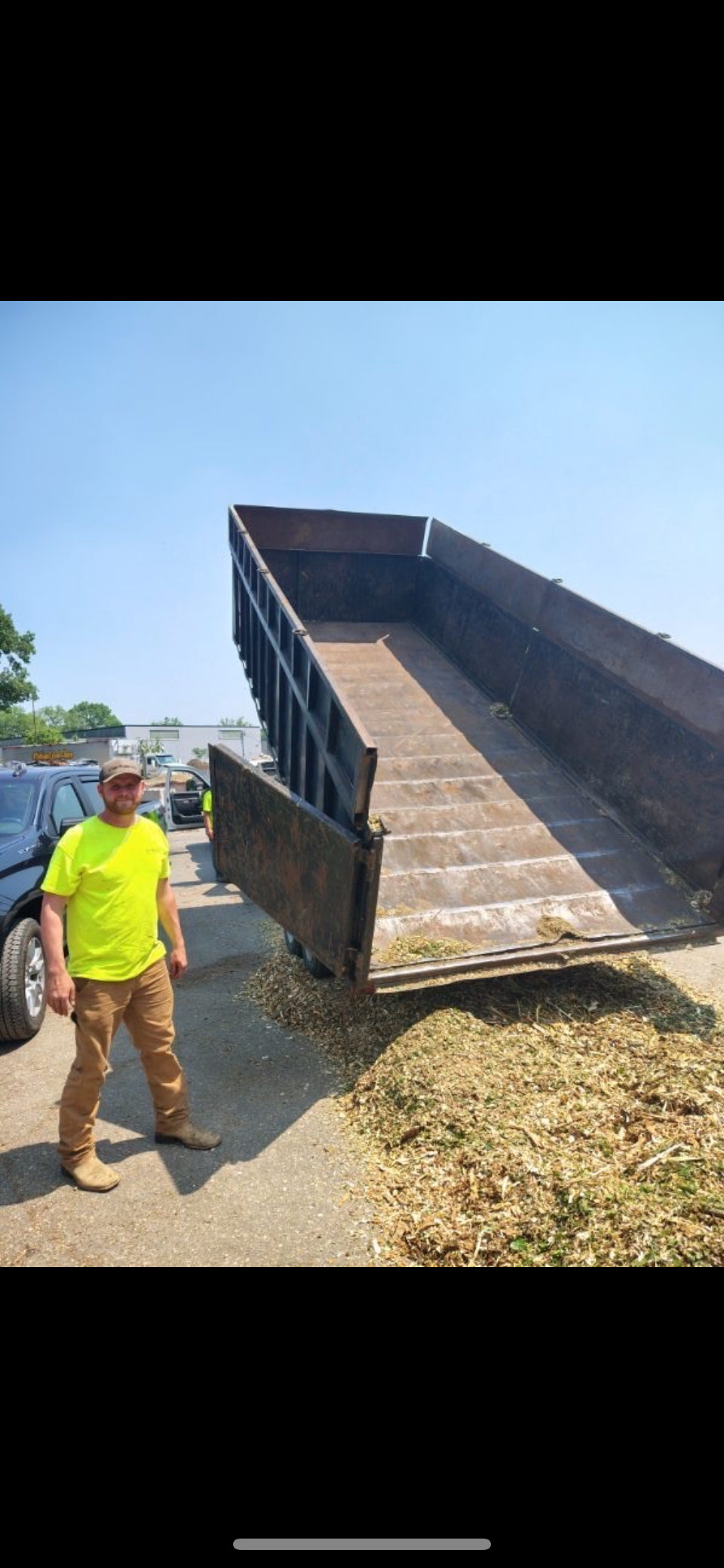 Worker in neon yellow shirt standing beside a raised dump truck bed on a gravel site under a clear sky