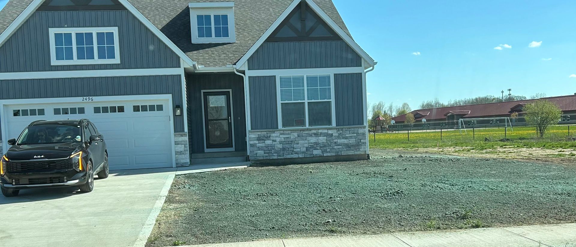 Single-story house under construction with a black car in the driveway and a gravel yard.