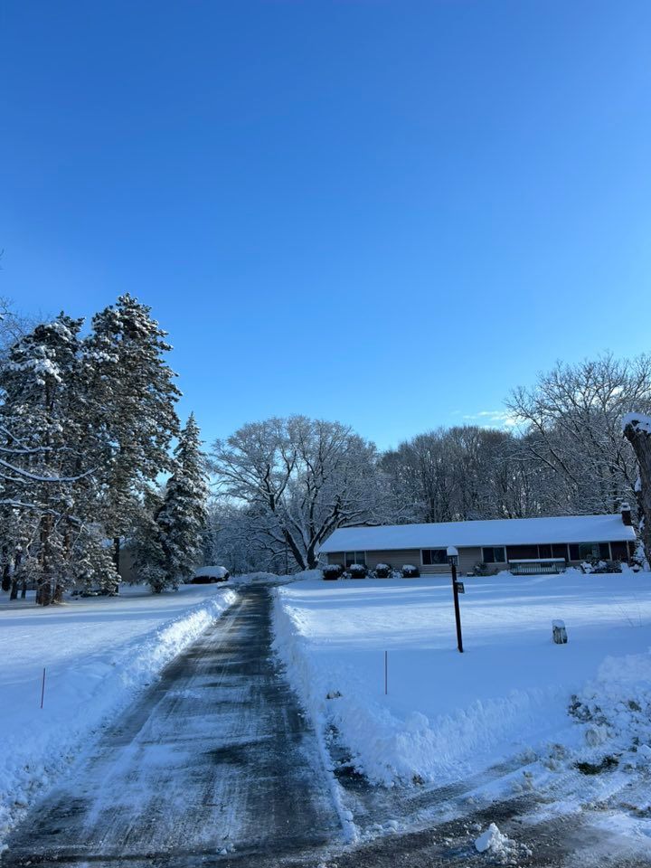 Snow-covered driveway leading to a house beneath a clear blue winter sky