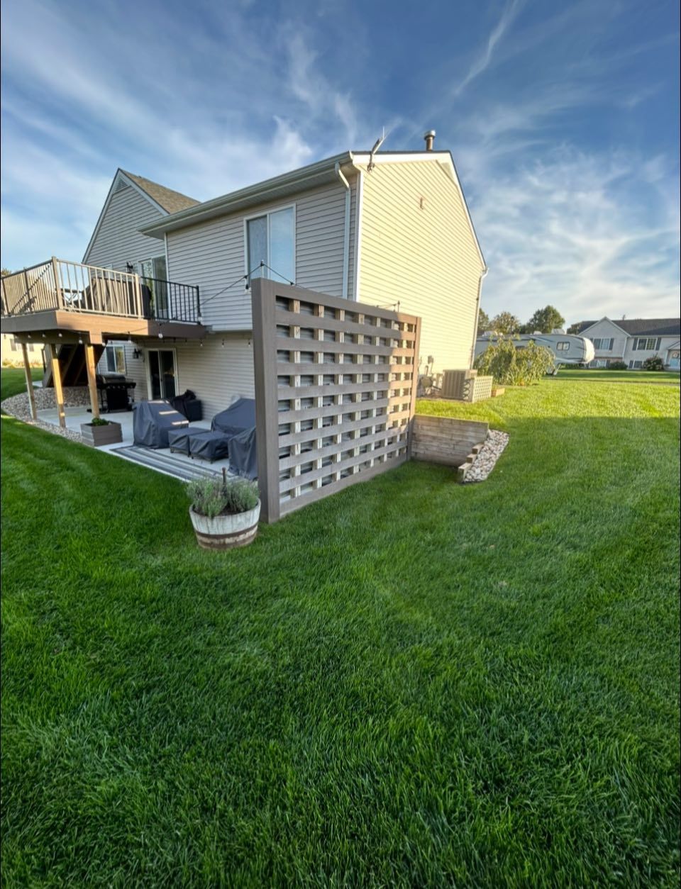 Backyard view of a beige two-story house with deck, lattice fence, and green lawn at sunset