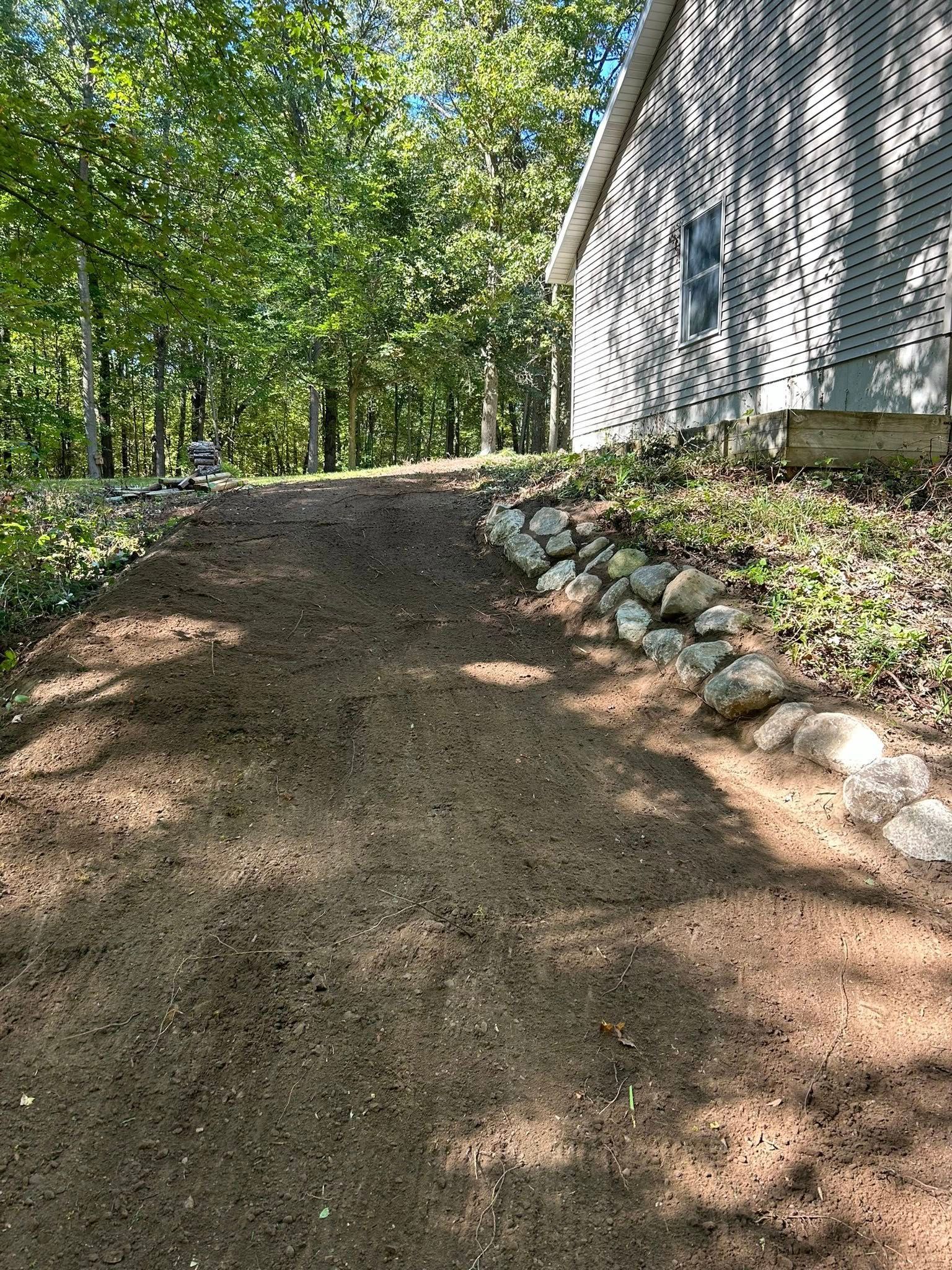 Gravel path sloping uphill beside a white house, with trees and sunlight in the background