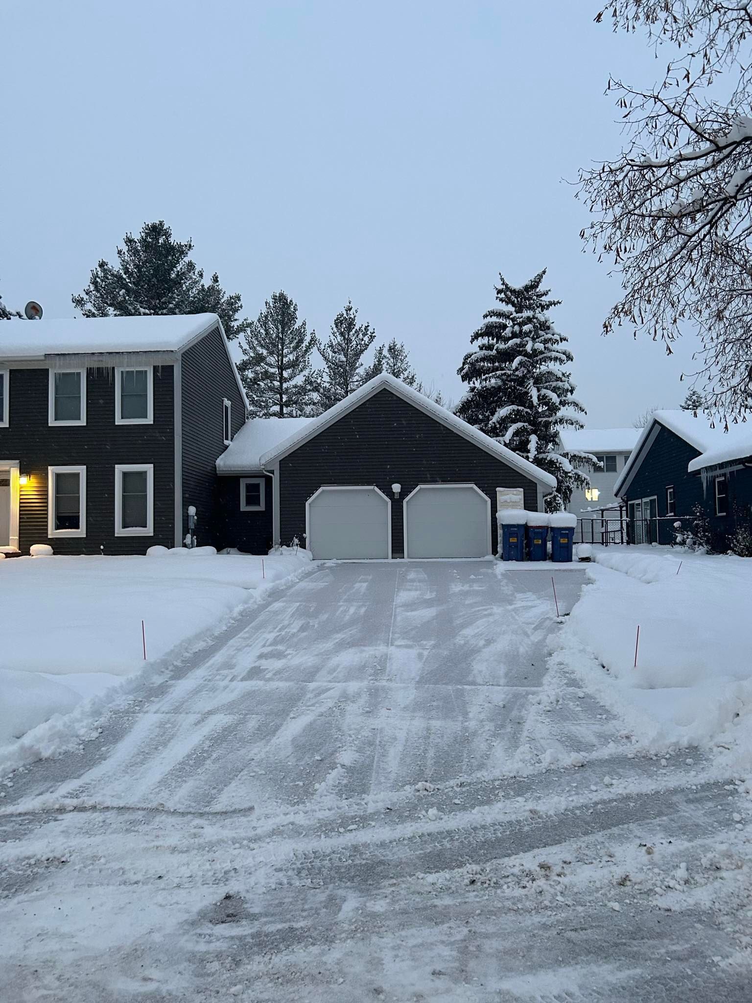 Snow-covered suburban house and garage with driveway tracks at dusk