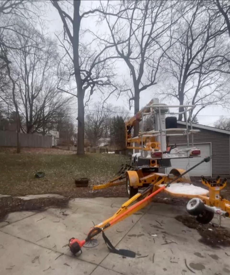 Orange utility boom lift parked on a concrete driveway beside a house and garage, with bare trees in the background
