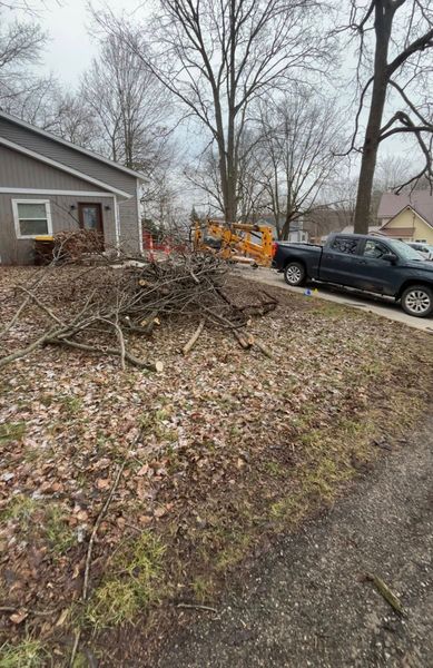 Front yard with a brush pile, black SUV, and yellow utility truck beside a house in late fall