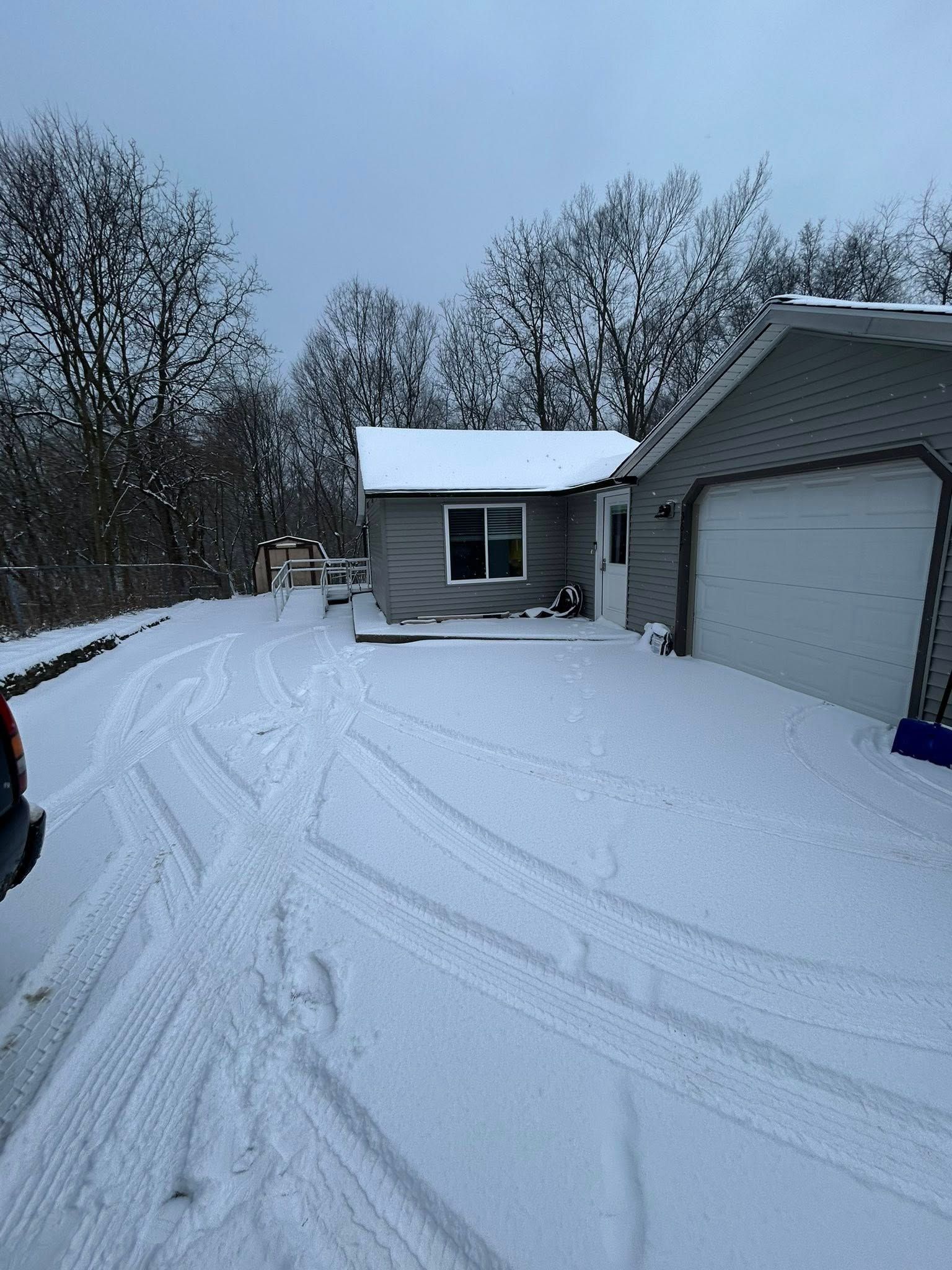 Snow-covered driveway beside a house and garage on a winter morning.