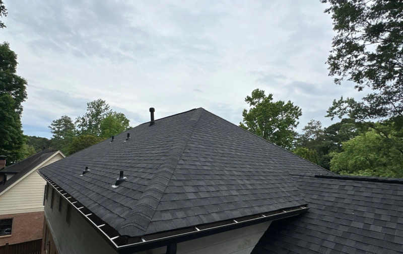 Dark gray shingle roof on a house, with a gutter and chimney, under a cloudy sky.
