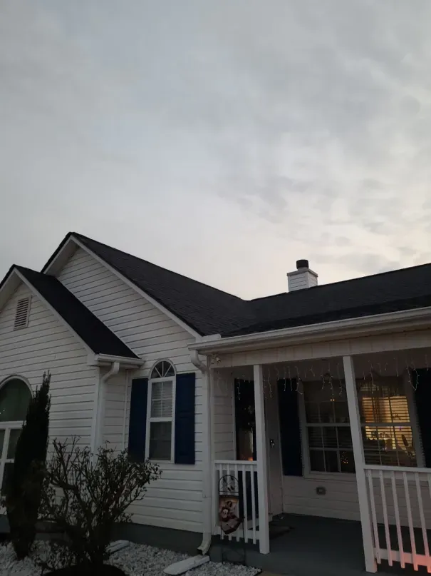 White house with dark roof and blue shutters against a cloudy sky.