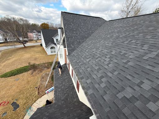 House exterior with brick, siding, and dark roof under a cloudy blue sky.