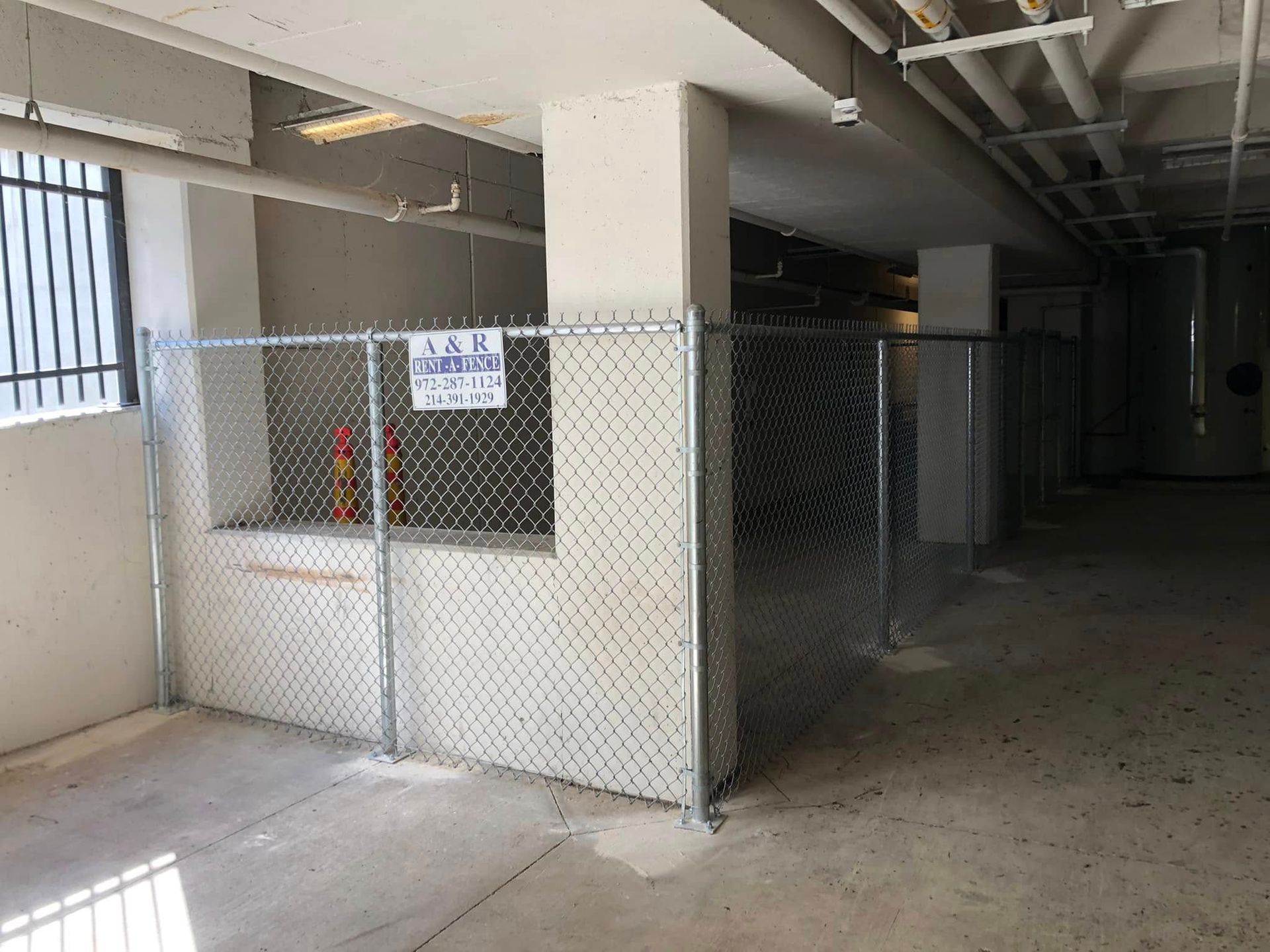 Chain-link fenced storage area in a dim concrete parking garage corridor.