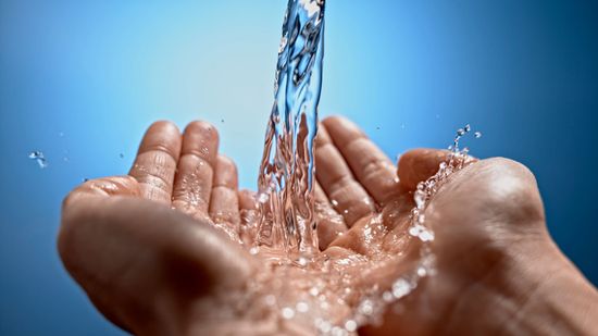 Hands cupped, catching a stream of clear water against a blue background.
