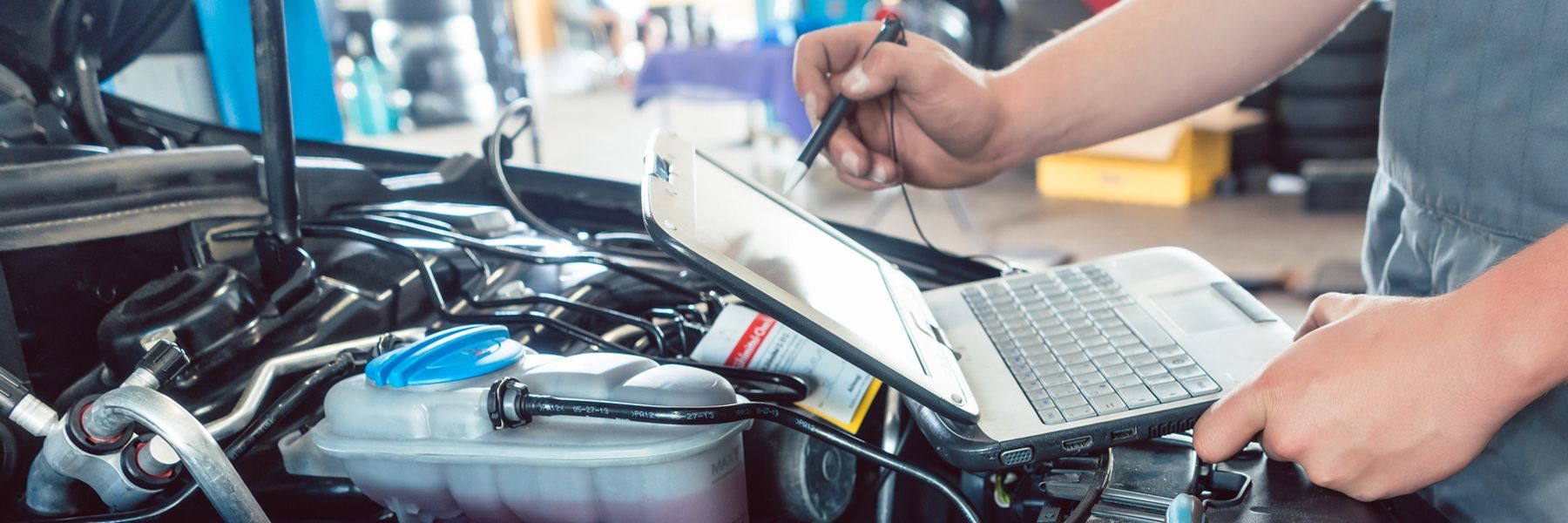 Mechanic using a laptop to diagnose a car engine in a garage