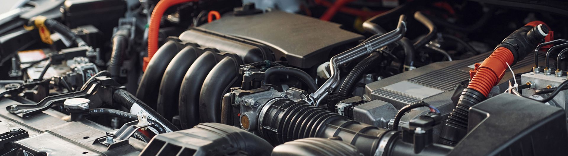 Car engine with exposed components, including tubes and wires. Red and black cables are visible.