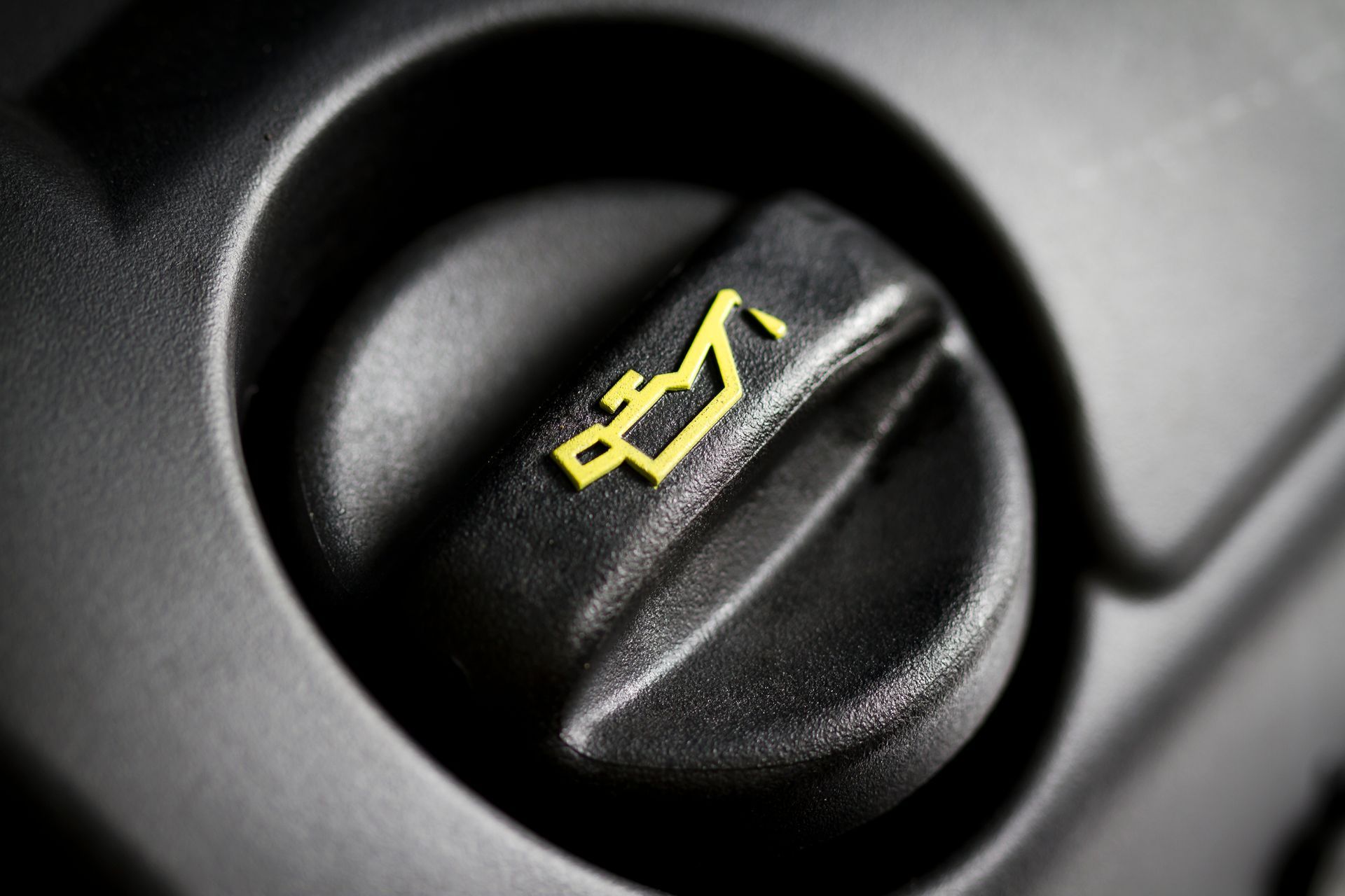 Close-up of a black engine oil cap with a yellow oil can symbol.