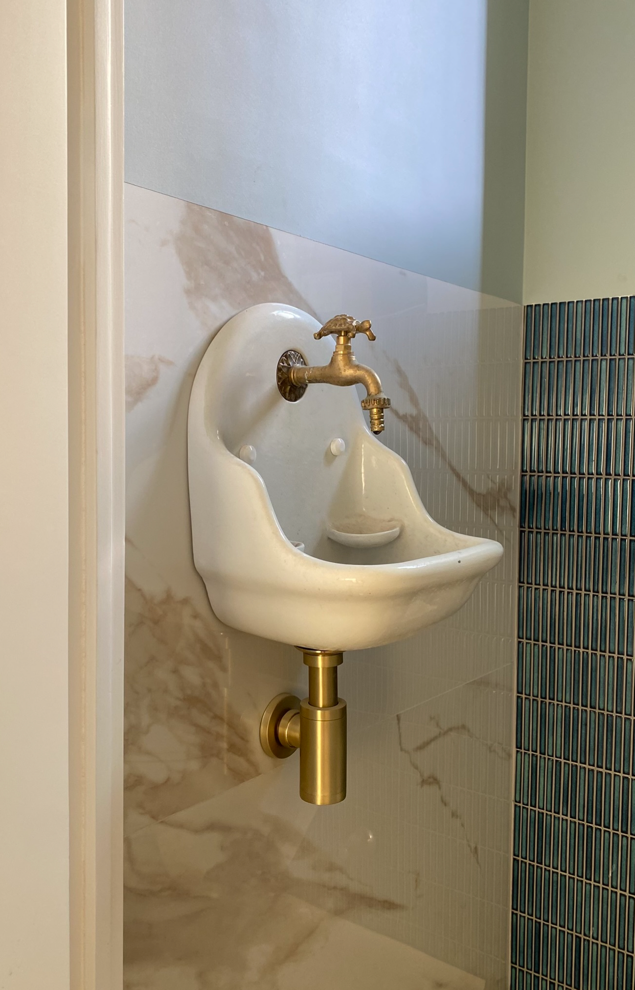 Witte, aan de muur gemonteerde antieke fontein met messing kranen op een marmeren muur.