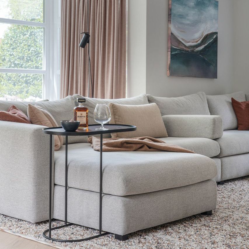 Gezellige woonkamer met een lichtgrijze hoekbank, een zwart bijzettafeltje met  neutrale kleuren.