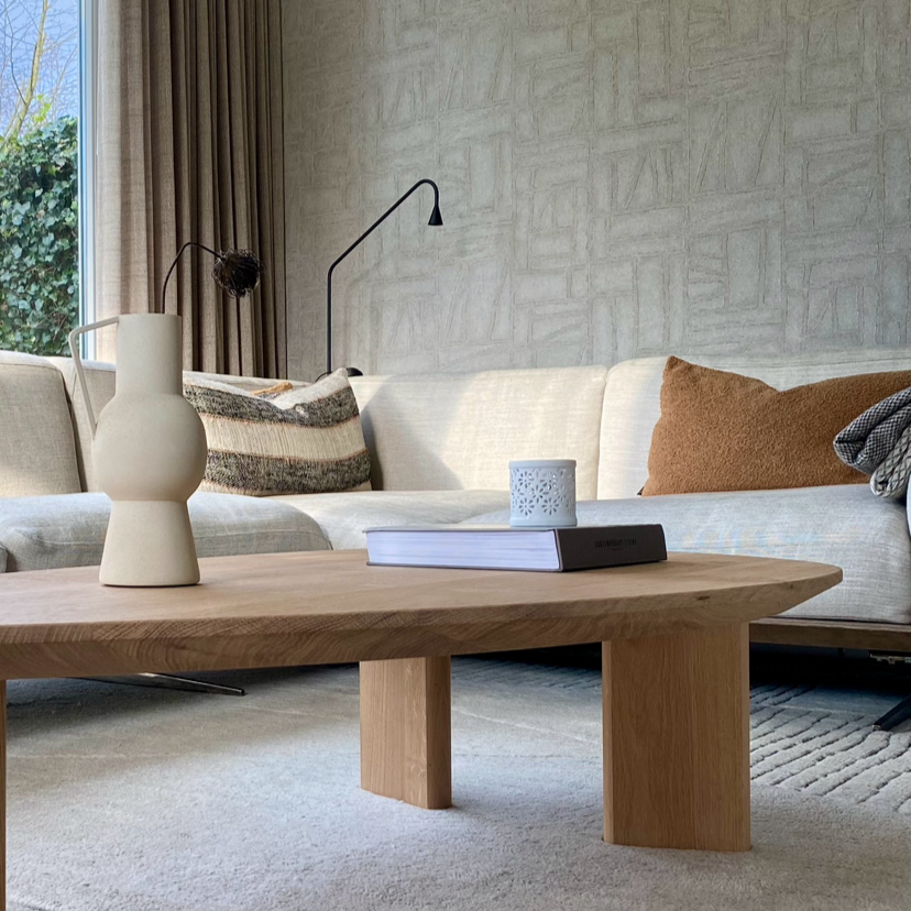 Woonkamer met crèmekleurige bank, houten salontafel, tapijt met patroon en behang in beige.