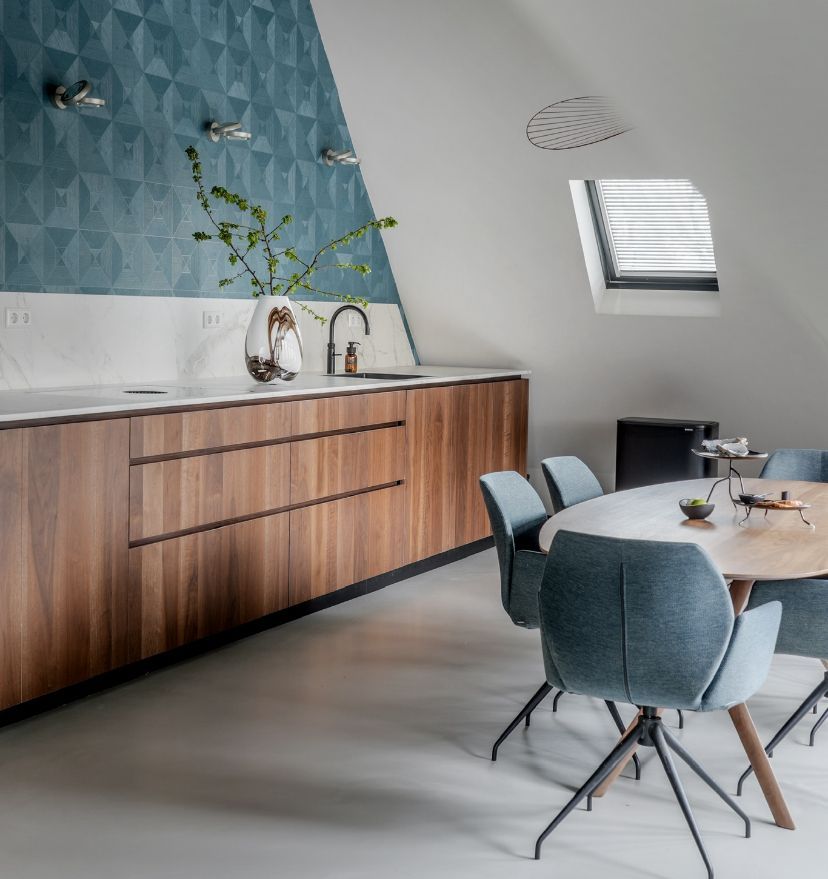 Moderne keuken met blauwe behang op de muur, walnoot houten kasten en een eettafel met blauwgroene stoelen.