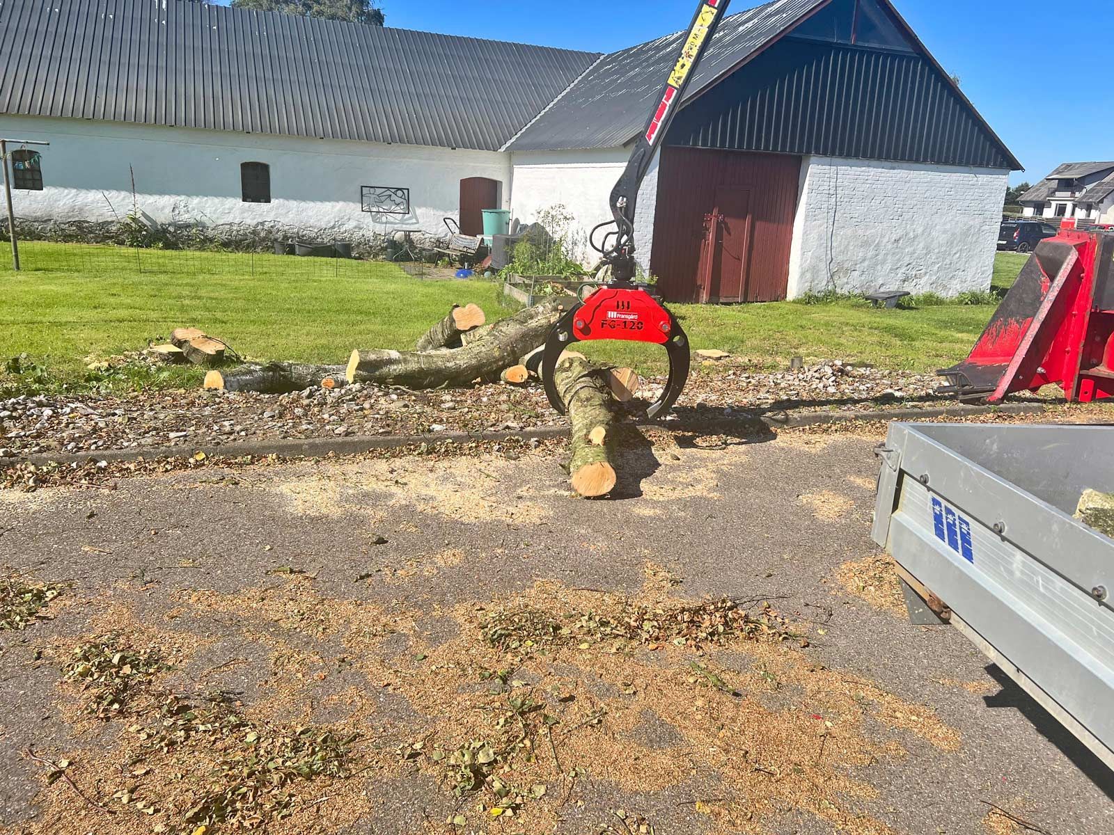 En skovgrab FG-120 løfter en gren foran et hus.