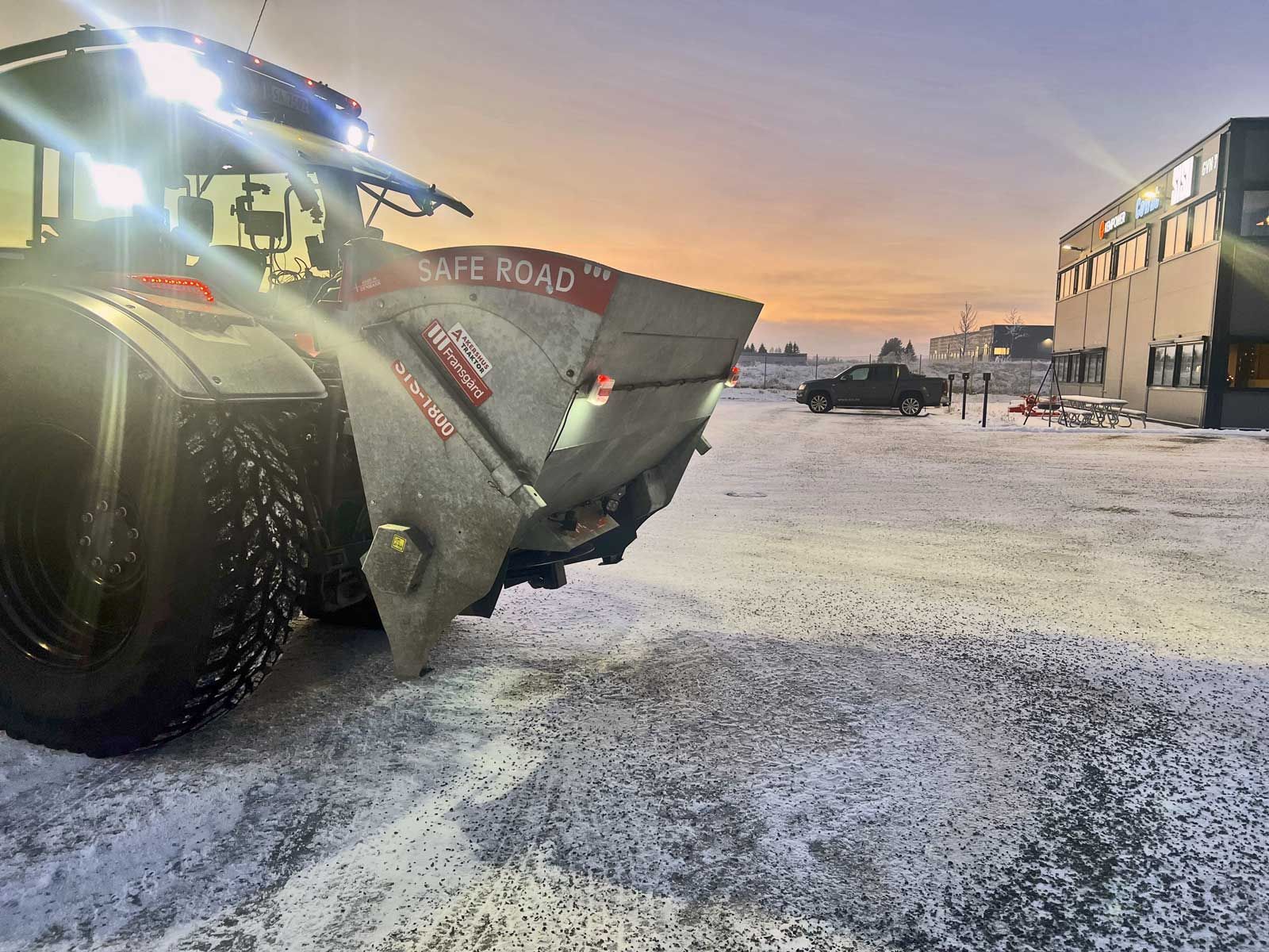 En traktor med en stor spreder kører på en parkeringsplads.