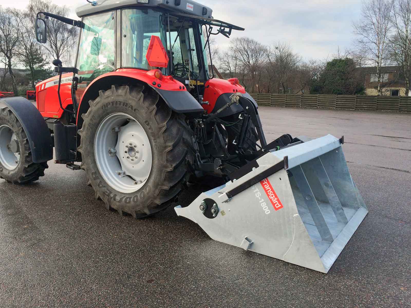En rød traktor med en selvlæssende spreder arbejder på en parkeringsplads.