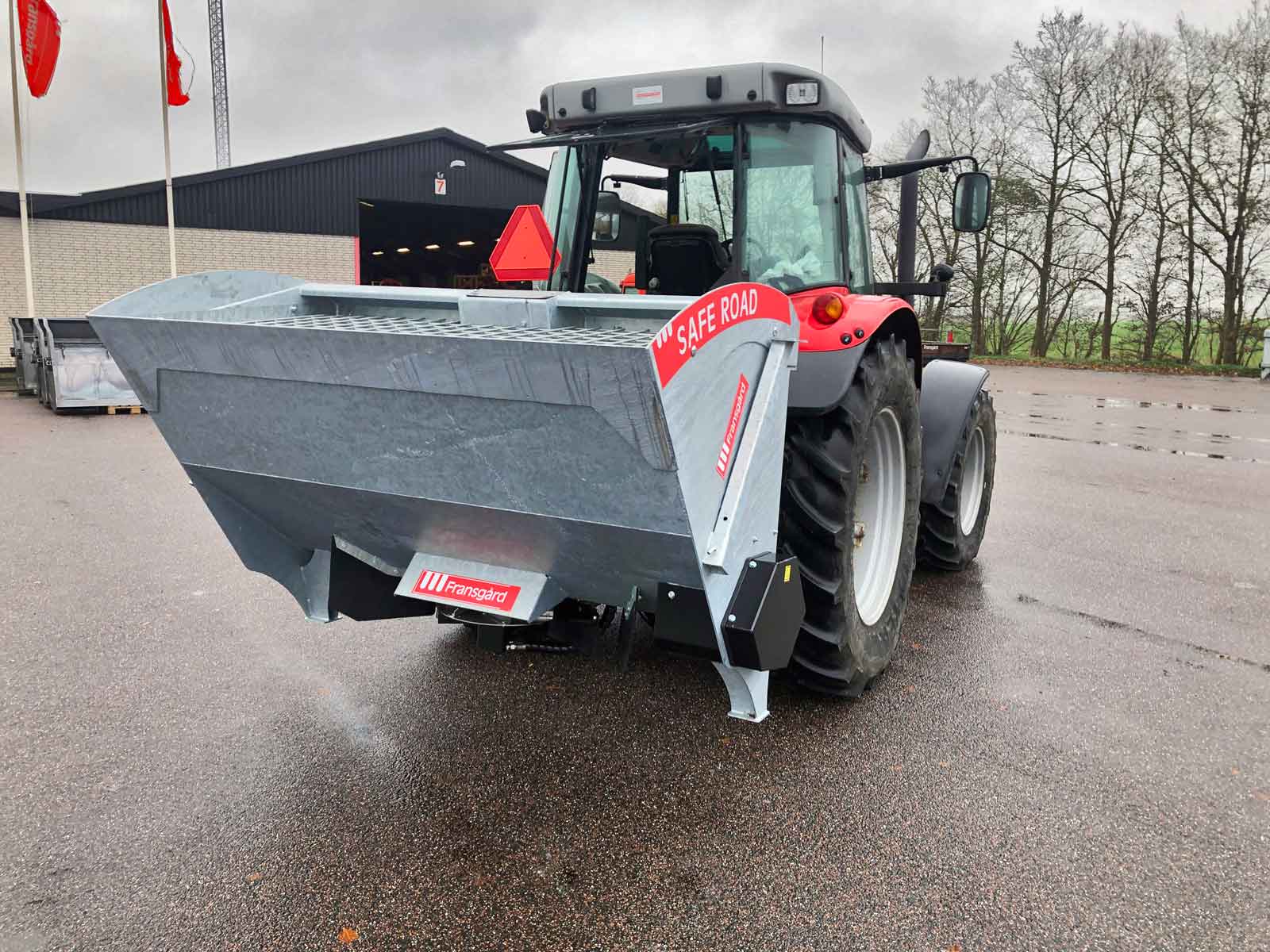 En rød og grå traktor har en spreder monteret bagpå.