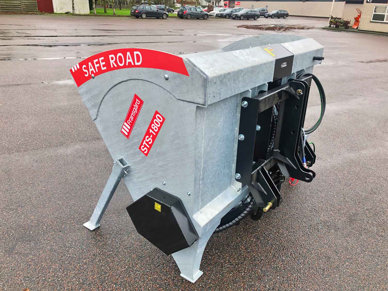 En galvaniseret spredemaskine står på jorden på en parkeringsplads.