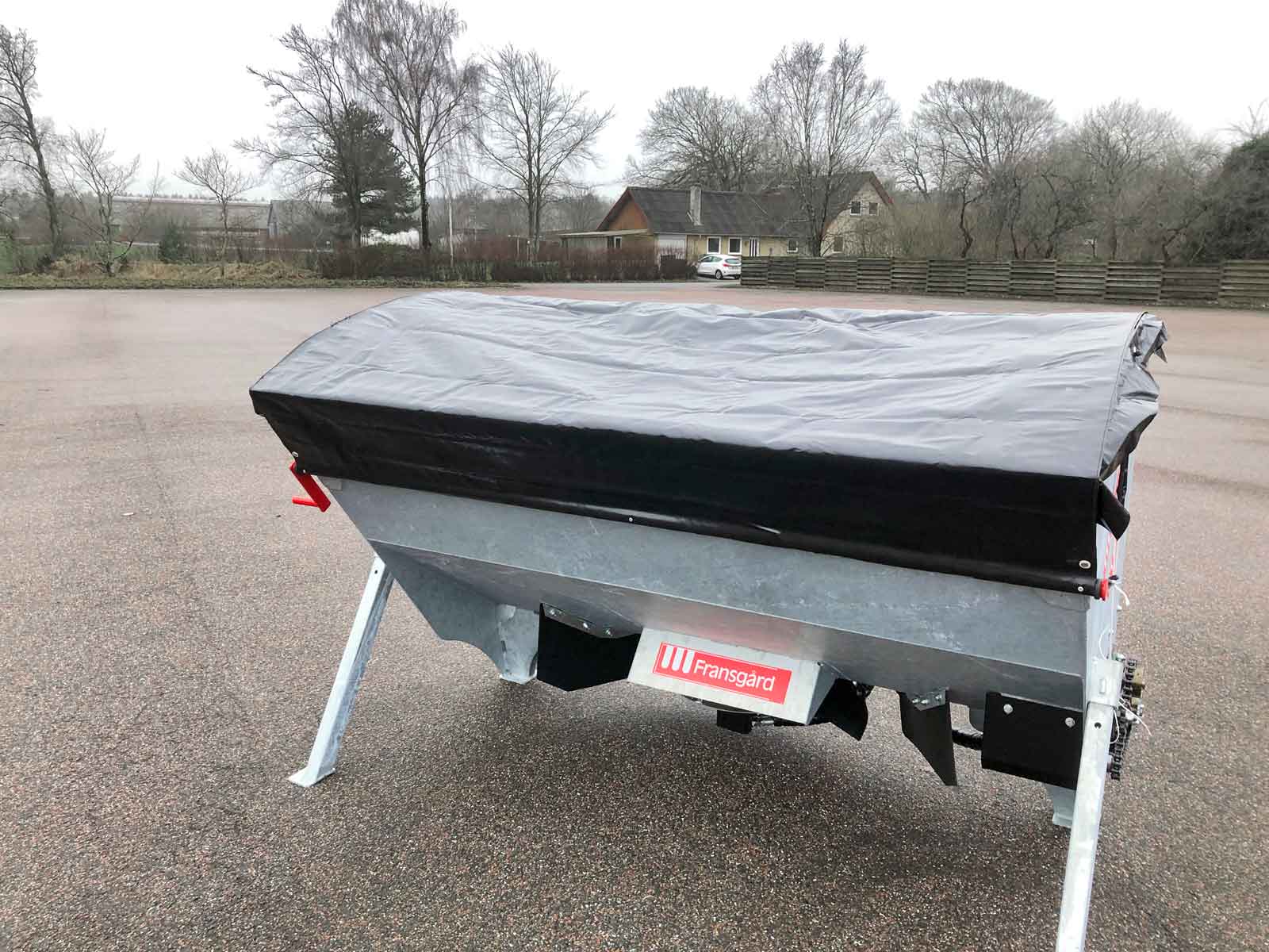En sort presenning dækker en spreder på en parkeringsplads.