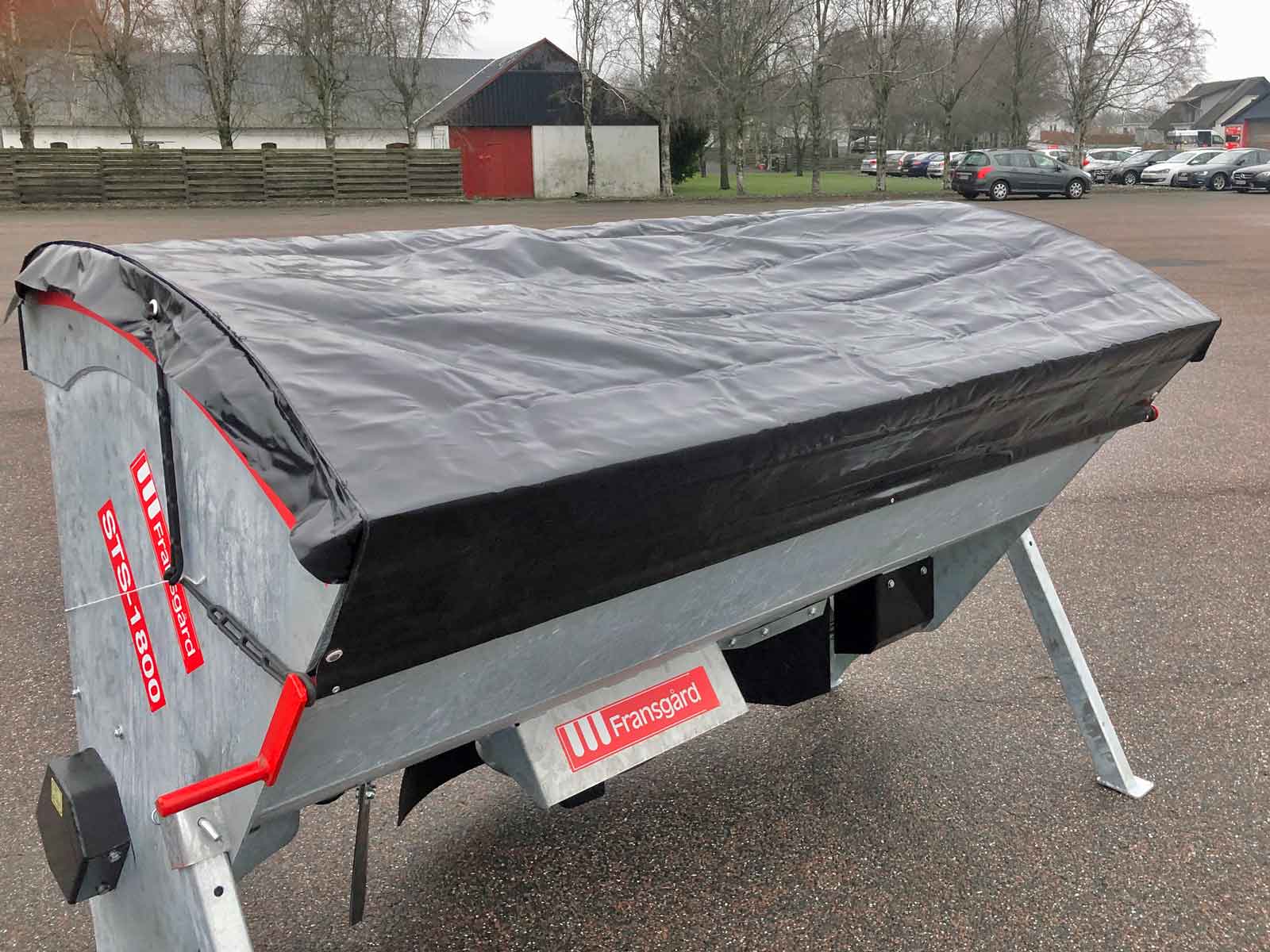 En tallerkenspreder med sort presenning ovenpå er parkeret på en parkeringsplads.