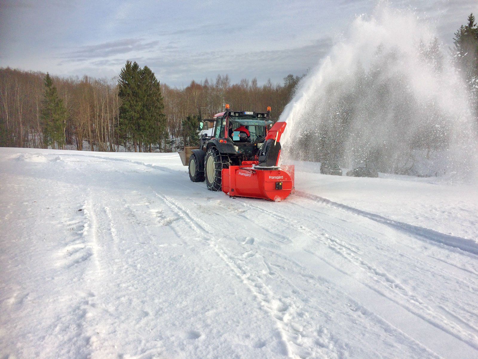 En traktor med en snefræser rydder sne på en snedækket vej.