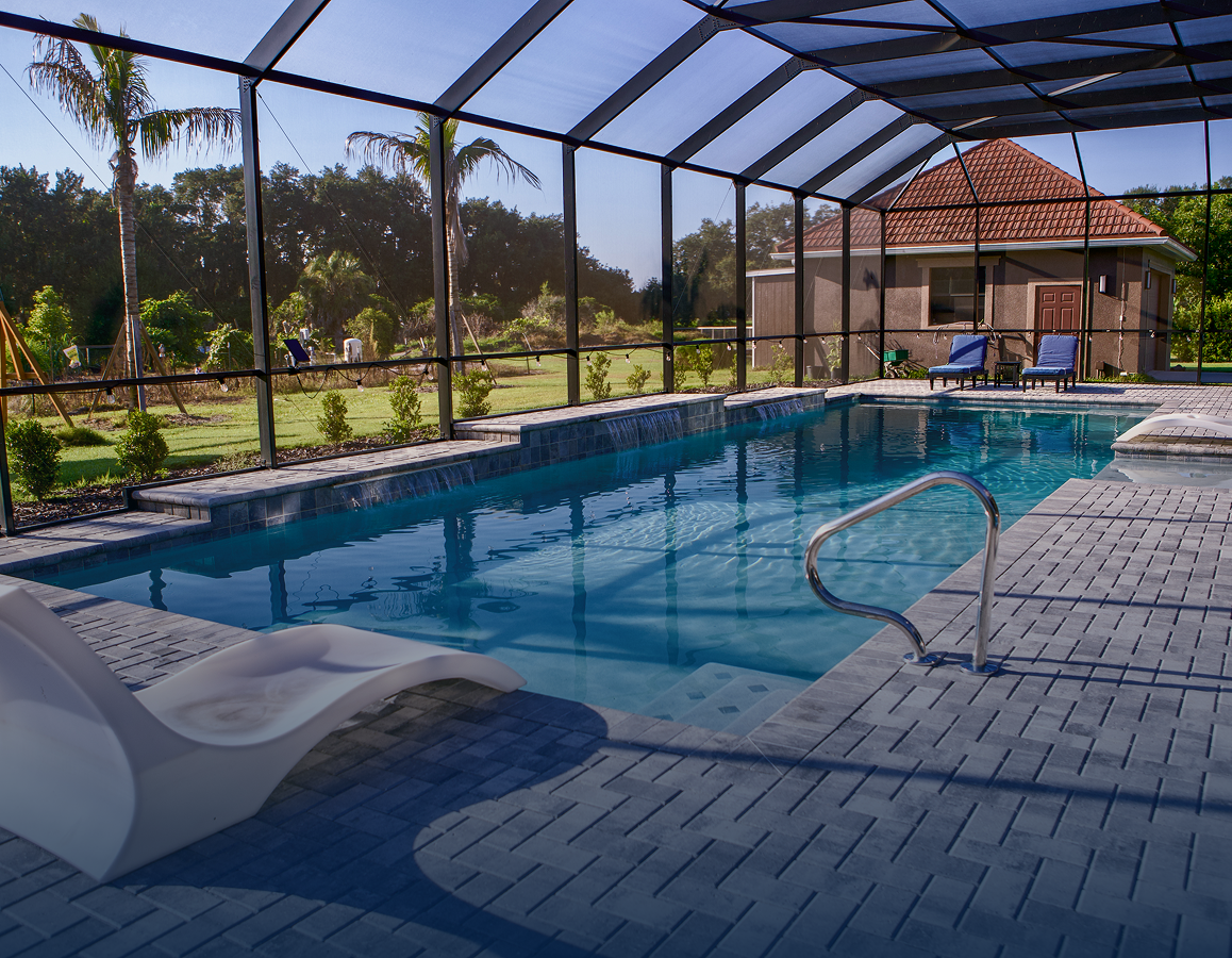 Covered backyard swimming pool with blue water, lounge chair, and screened enclosure beside a house
