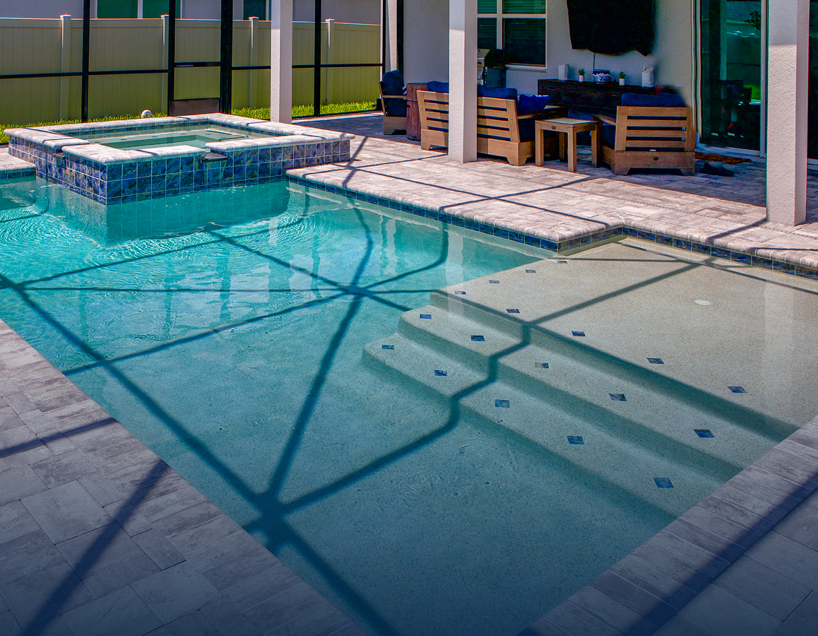 Modern backyard swimming pool with steps, hot tub, and patio seating in bright sunlight